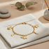 14k gold-filled bracelet adorned with elephant and Figa hand charms rests on beige cloth, surrounded by stones, leaves, and incense.